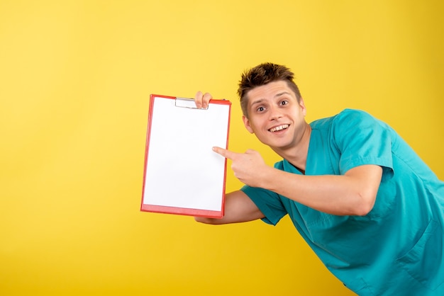 Front view young male doctor in medical suit with note and analysis on yellow background