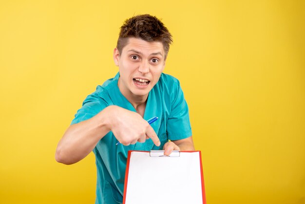 Front view young male doctor in medical suit with note and analysis on yellow background