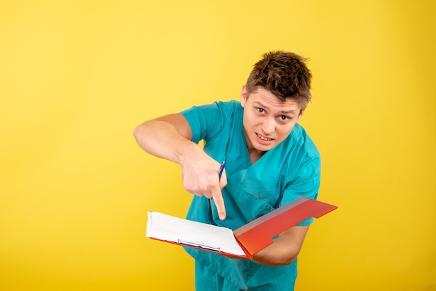 Front view young male doctor in medical suit with notes on the yellow background