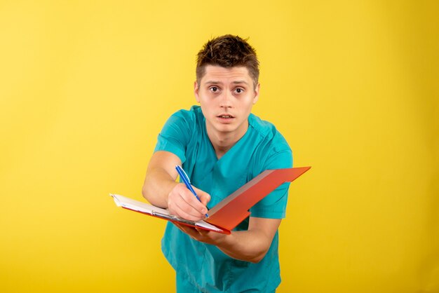 Front view young male doctor in medical suit with notes on yellow background