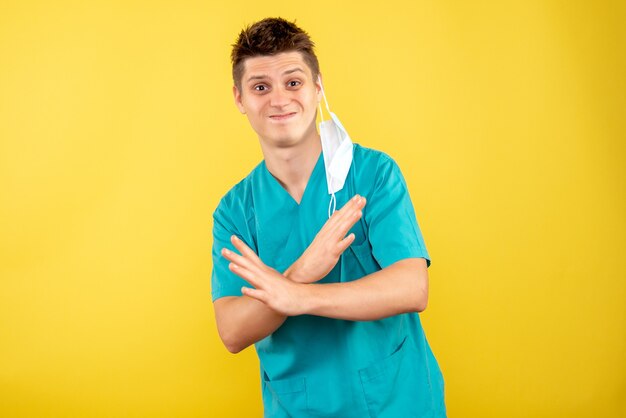 Вид спереди молодой мужчина-врач в медицинском костюме со стерильной маской на желтом фоне