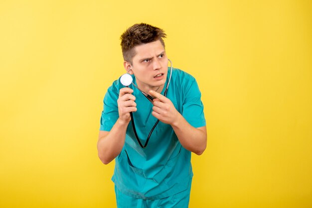 Front view young male doctor in medical suit with stethoscope on the yellow background