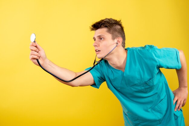 Вид спереди молодой мужчина-врач в медицинском костюме со стетоскопом на желтом фоне
