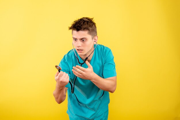 Front view young male doctor in medical suit with stethoscope on yellow desk