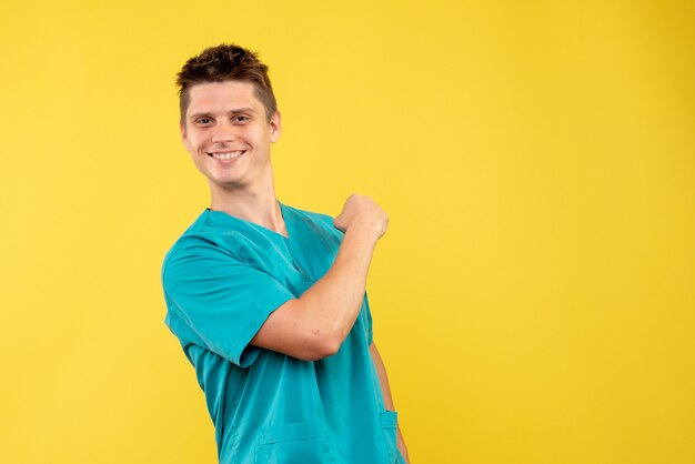 Front view young male doctor in medical suit on a yellow background