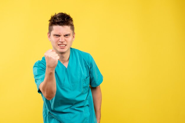 Front view young male doctor in medical suit on a yellow background
