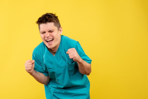 Front view young male doctor in medical suit on the yellow background