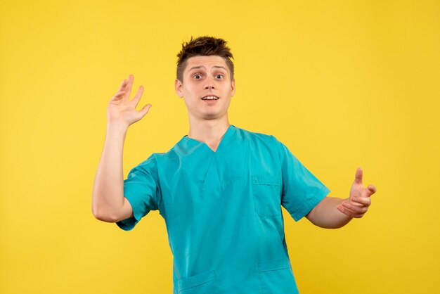Front view young male doctor in medical suit on yellow background