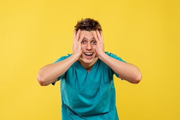 Front view young male doctor in medical suit on yellow background