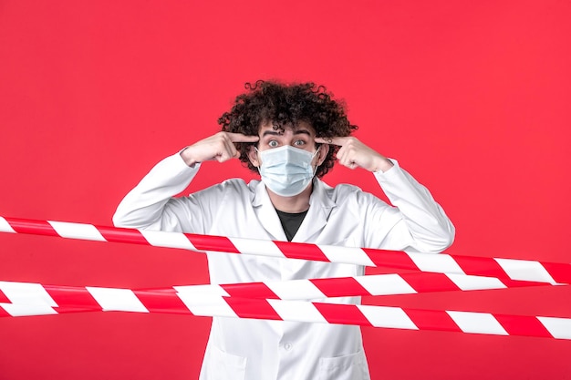 Free photo front view young male doctor in medical uniform and mask on red background danger covid- health quarantine warning hospital