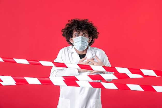 Front view young male doctor in medical uniform and mask on red background danger isolation hospital covid- health quarantine warning strip