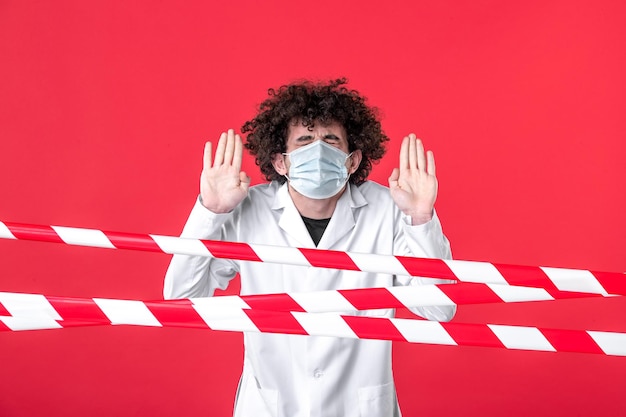 Foto gratuita vista frontale giovane medico maschio in uniforme medica e maschera su sfondo rosso isolamento ospedale farmaco covid- avvertenza pericolo di quarantena