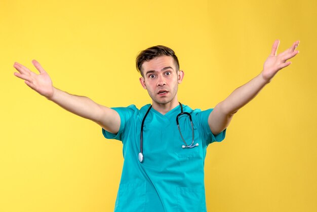 Front view of young male doctor posing on yellow wall