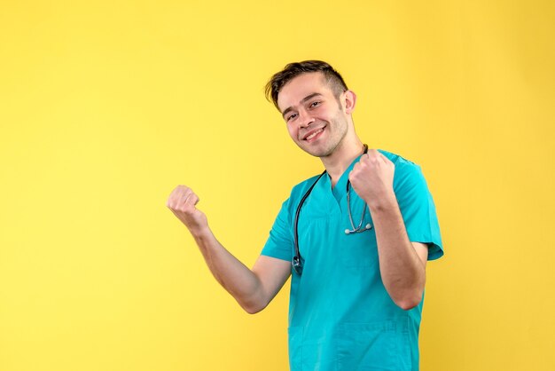 Front view of young male doctor smiling on yellow wall