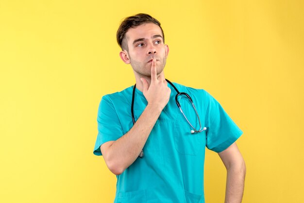 Front view of young male doctor thinking on yellow wall