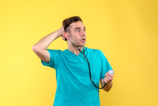 Вид спереди молодого мужчины-врача с помощью стетоскопа на желтой стене