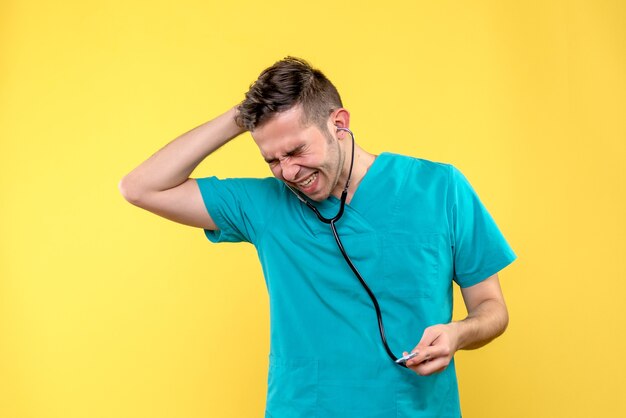 Front view of young male doctor using stethoscope on yellow wall