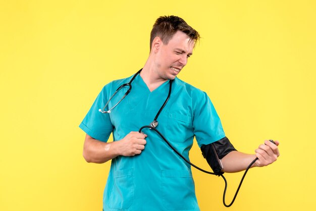 Front view of young male doctor using tonometer on yellow wall