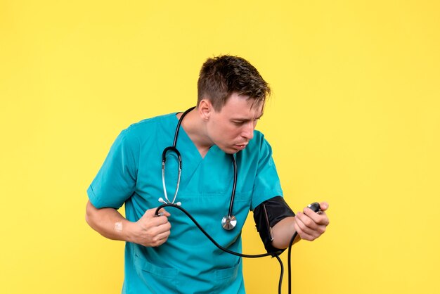 Front view of young male doctor using tonometer on yellow wall