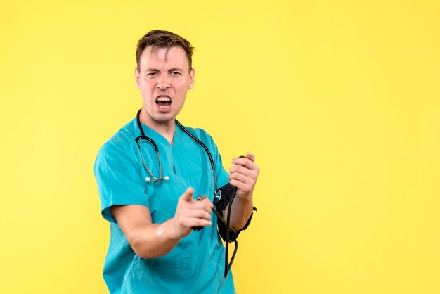 Front view of young male doctor using tonometer on yellow wall