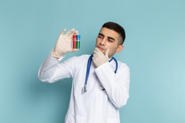 Front view of young male doctor in white suit with blue stethoscope holding flasks