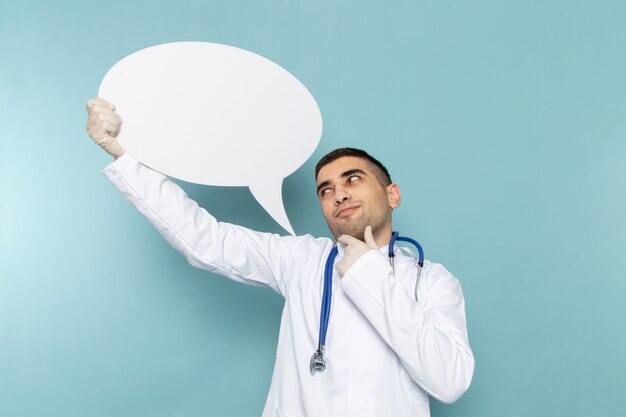 Front view of young male doctor in white suit with blue stethoscope holding white sign