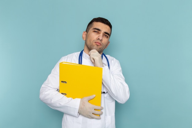 Front view of young male doctor in white suit with blue stethoscope holding yellow files