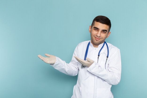 Front view of young male doctor in white suit with blue stethoscope posing and smiling