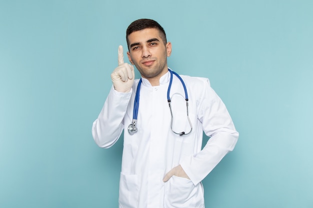 Front view of young male doctor in white suit with blue stethoscope posing