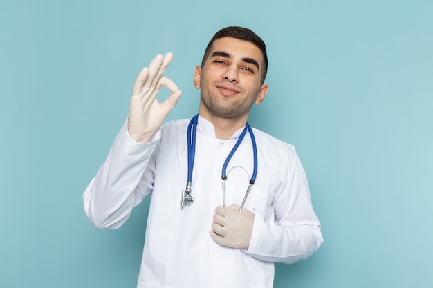 Front view of young male doctor in white suit with blue stethoscope smiling and posing