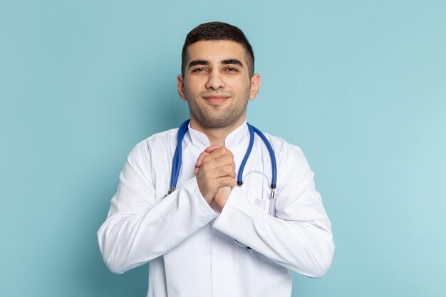 Front view of young male doctor in white suit with blue stethoscope smiling posing