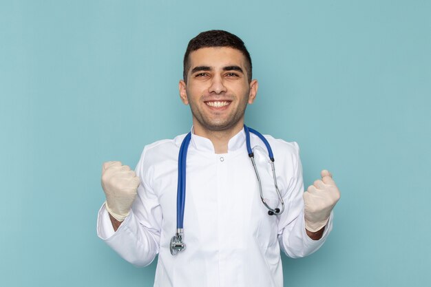 Вид спереди молодого мужчины-врача в белом костюме с синим стетоскопом улыбается