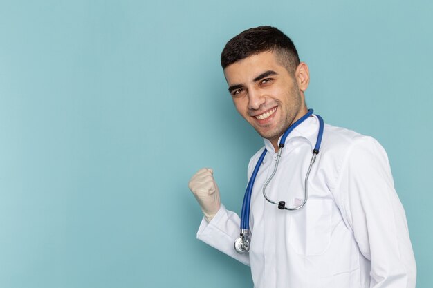 Front view of young male doctor in white suit with blue stethoscope smiling