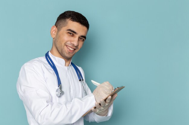 メモを書く青い聴診器で白いスーツの若い男性医師の正面図