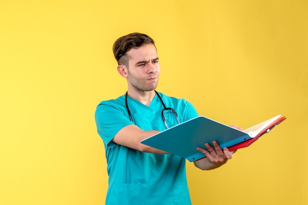 Front view of young male doctor with analyzes on yellow wall