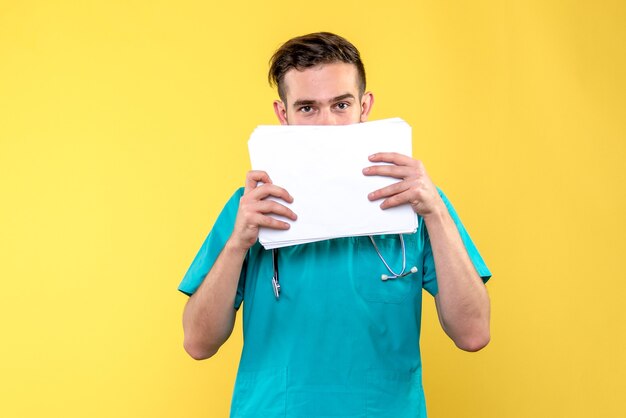 Front view of young male doctor with documents on a yellow wall