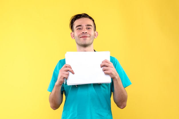 Front view of young male doctor with documents on the yellow wall