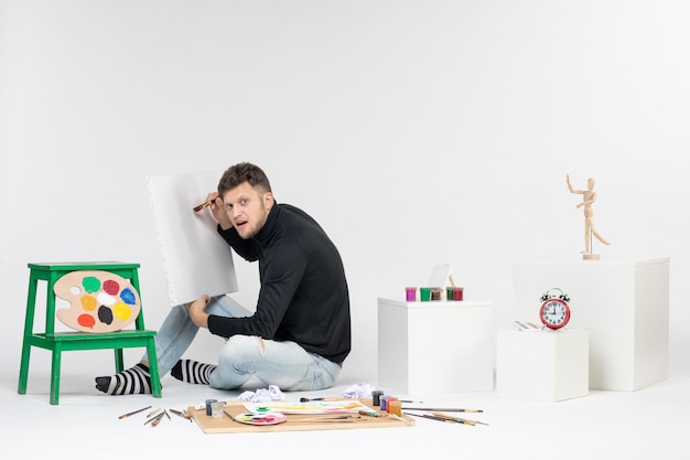 Вид спереди молодой мужчина рисунок картина с кисточкой на белой стене искусство цветная картина краска краска рисунок художник