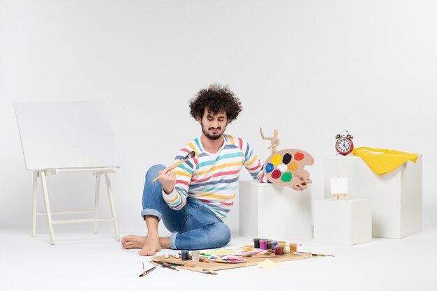 Front view of young male drawing paintings on a white wall