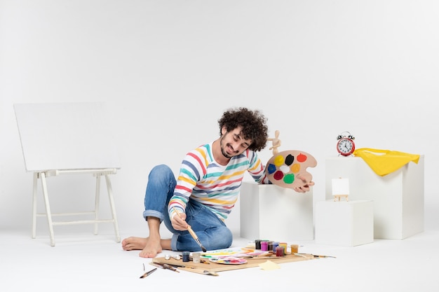 Front view of young male drawing paintings on white wall