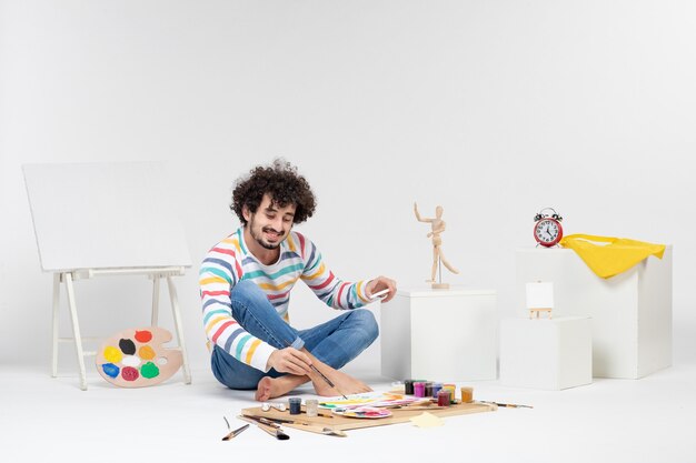 Front view of young male drawing pictures with paints on the white wall