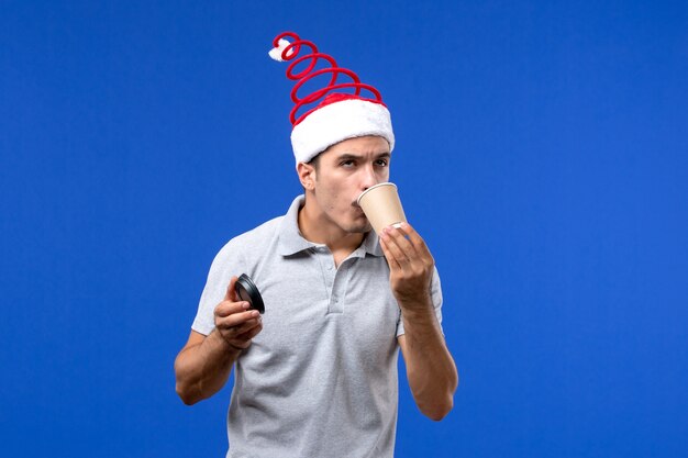 Front view young male drinking coffee on blue wall new year male holiday emotion