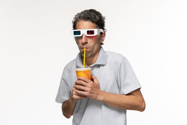 Вид спереди молодого мужчины, пьющего соду и смотрящего фильм в солнцезащитных очках d на белой поверхности