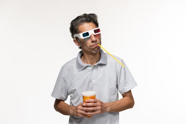 Вид спереди молодого мужчины, пьющего соду и смотрящего фильм в солнцезащитных очках d на белой поверхности
