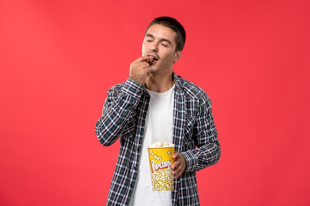 Free photo front view young male eating popcorn on light-red wall cinema theater film movie