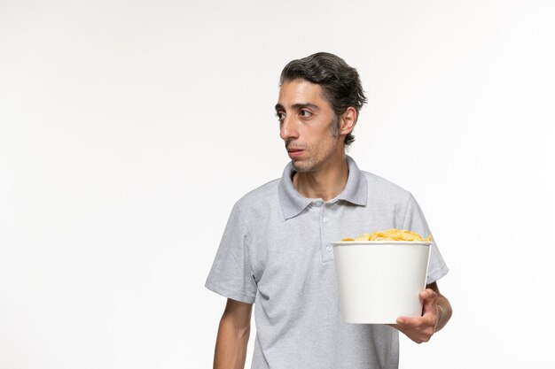 正面図明るい白い表面でポテトチップスを食べる若い男性