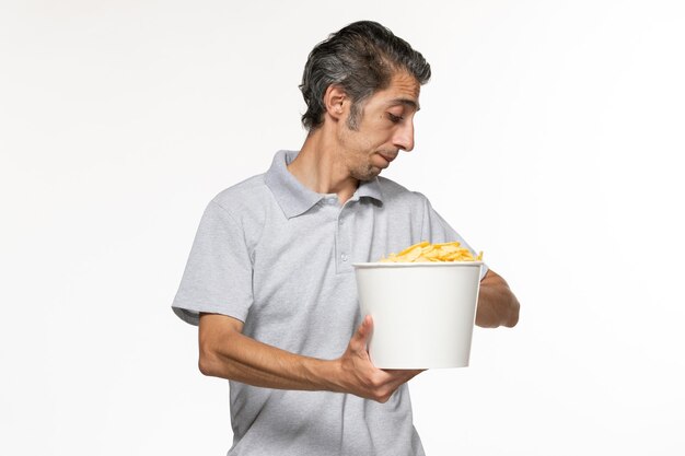 白い表面で彼の手首を見て映画を見ながらポテトチップスを食べる若い男性の正面図