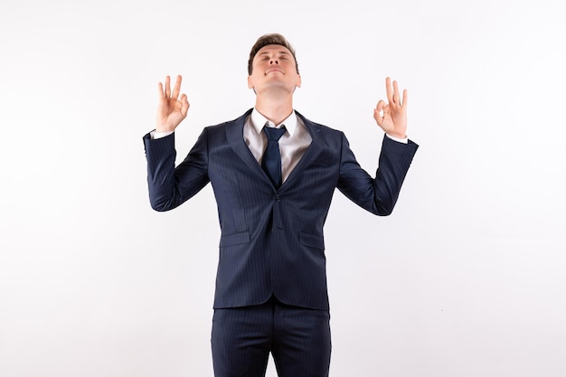 Front view young male in elegant classic suit in meditation pose on white background