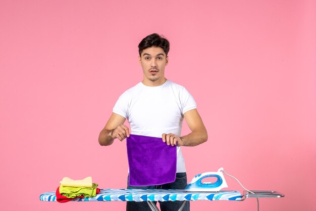 Вид спереди молодой мужчина складывает чистые полотенца на розовом