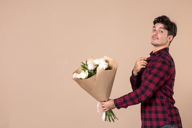 Front view young male giving beautiful flowers on brown wall